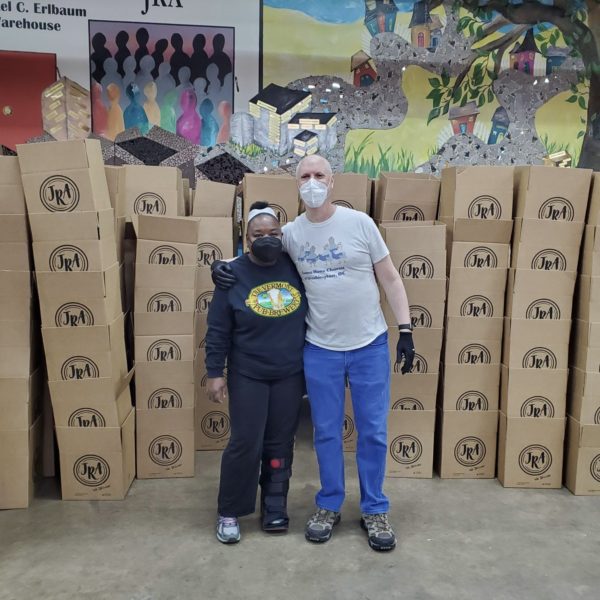 woman and man standing with arm around each other in front of stacks of boxes to be filled with food